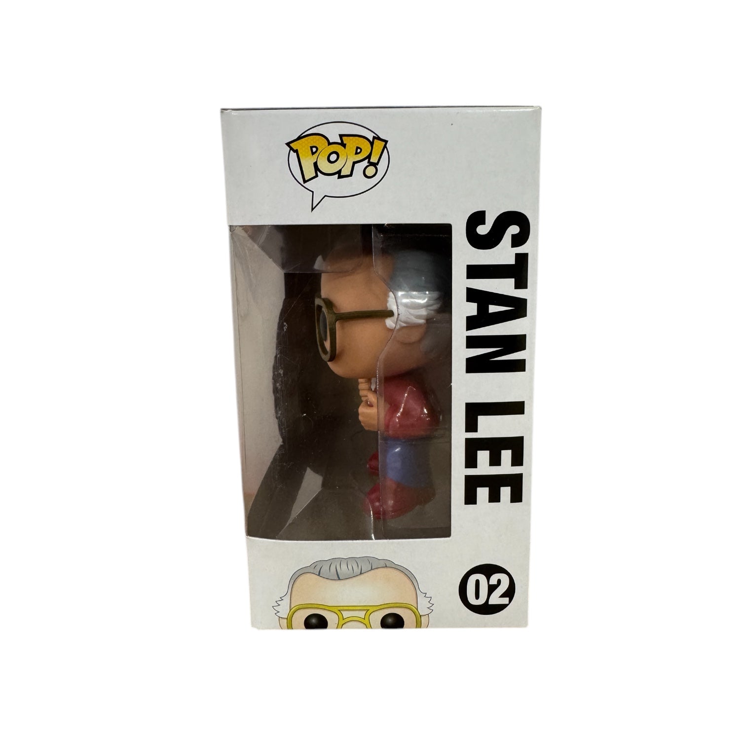 Stan Lee standing with his hands pulling apart a red jumper showing a white t-shirt that says 'Fan Expo' wearing red boots.